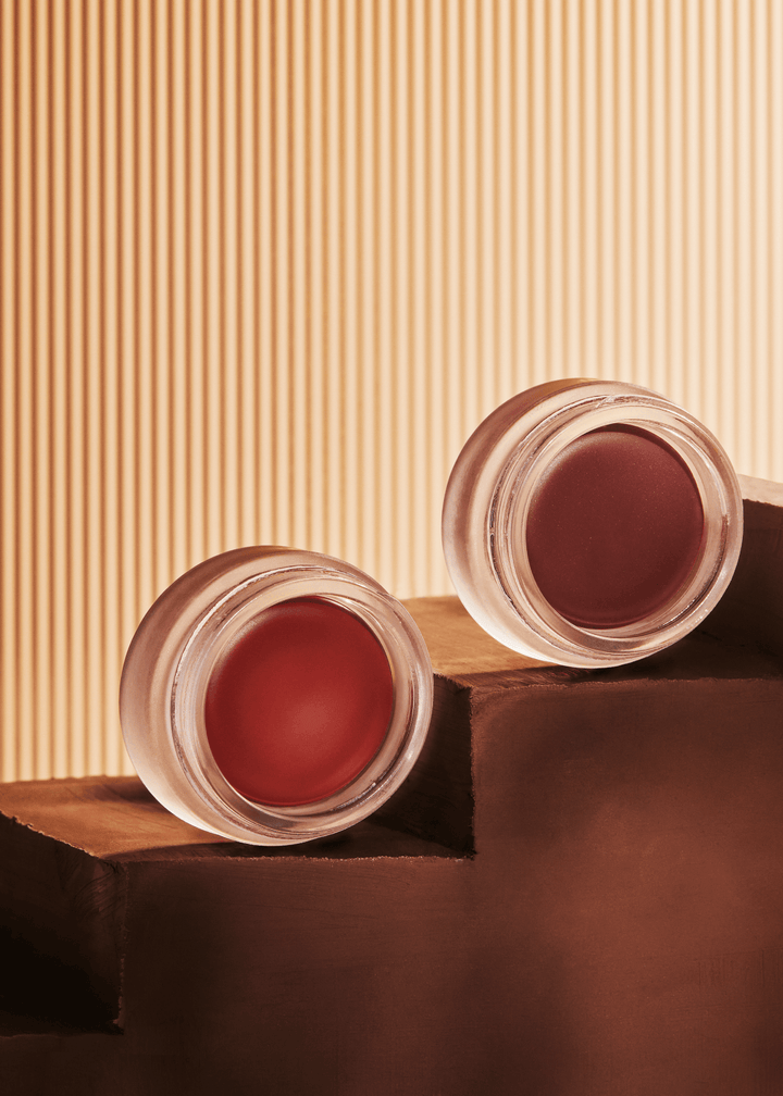 Two glass pots with cream blush. A red cream blush in shade Scarlet, and mauve cream blush in shade Orchid from beauty brand Minori